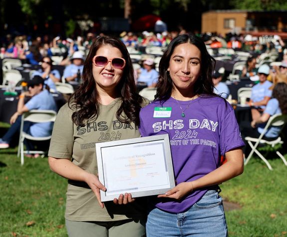 two students stand together holding an award