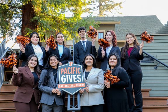 A group of students hold an orange 'Pacific Gives' sign while shaking pom-poms.  