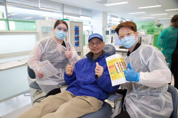 male senior patient in the center with one dental student posed on either side with dental information