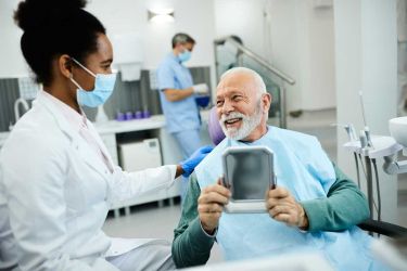 smiling senior aged man holding a mirror and looking at the dentist