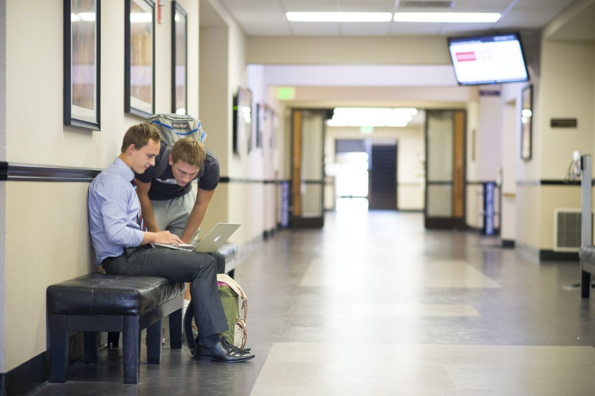 business students look at a laptop in the hallway of Weber Hall
