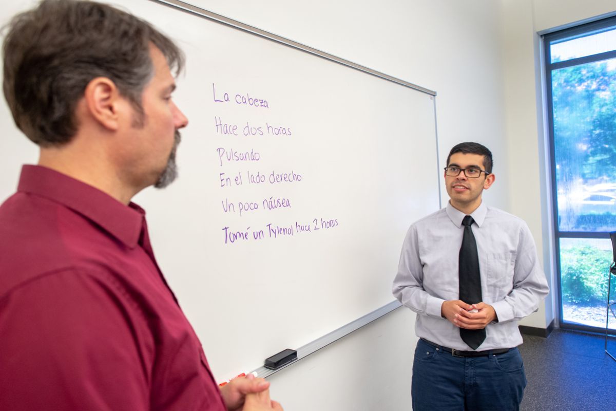 student and professor talking in front of white board with Spanish phrases