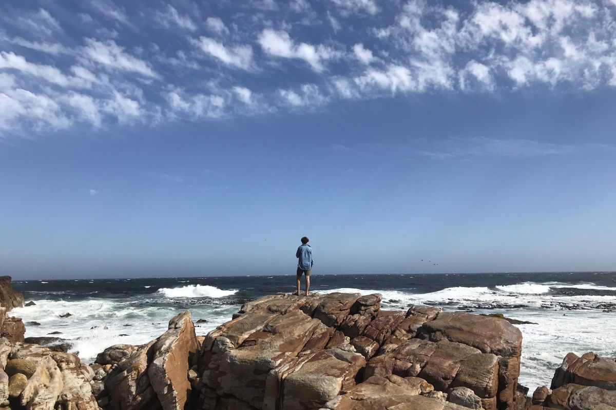 a student stands on rocks looking at waves