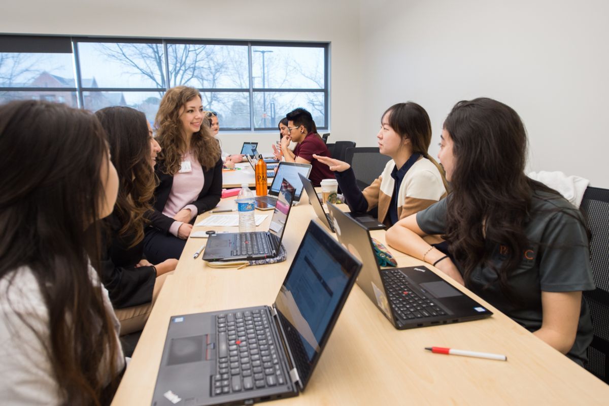 Photo shows 5 PA students sitting and talking in front of their laptops.  