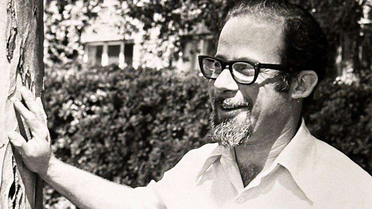 A man wearing glasses stands next to a tree