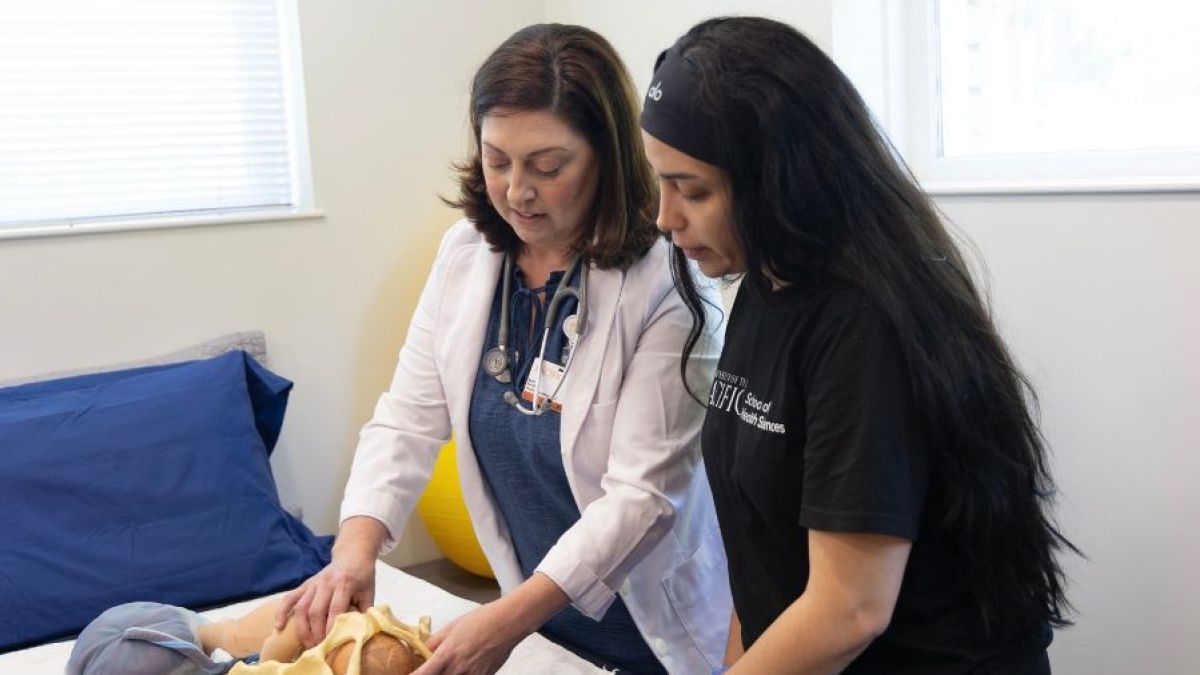 A professor showing a students a midwifery technique with a model 