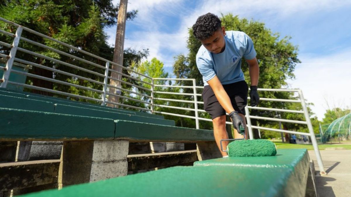 A student adds fresh green paint to a bench 