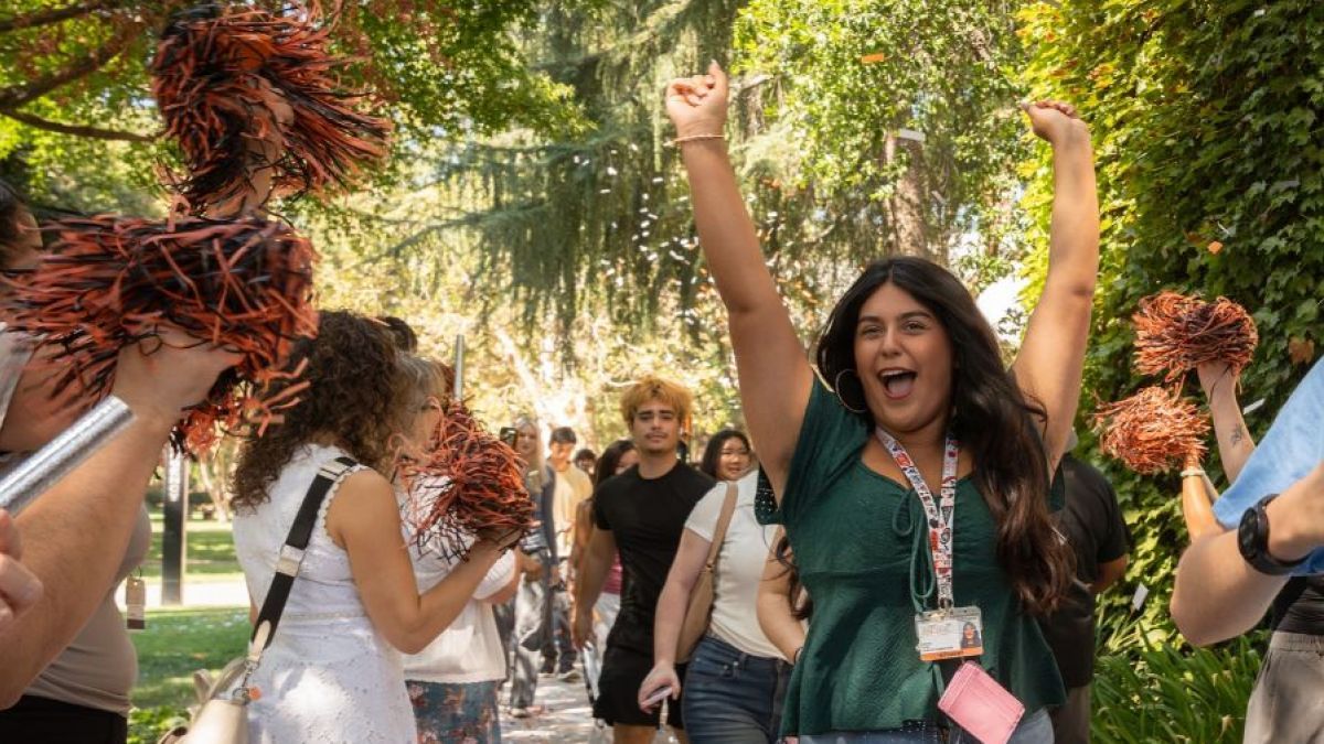 A student cheers in a green shirt surrounded by confetti 