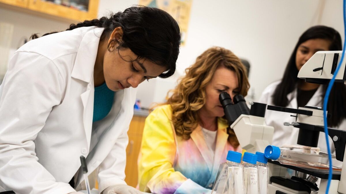A student in a white lab coat writes in a notebook