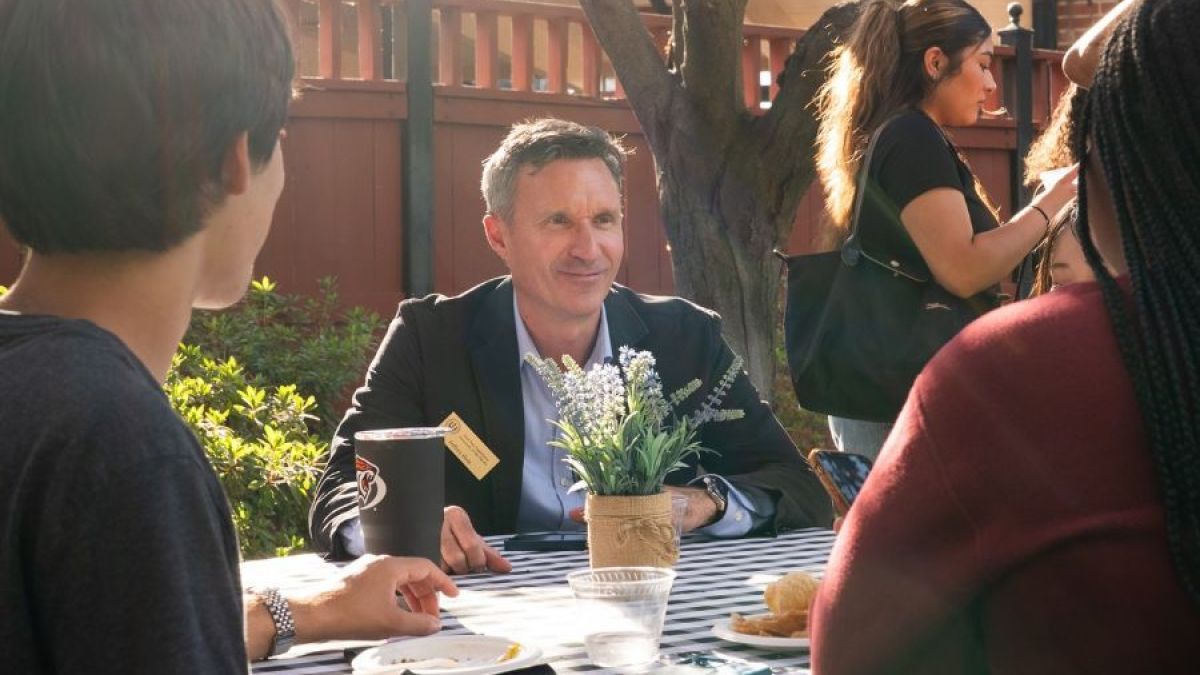 Professor Jeff Hole sits at a table outside with two students 