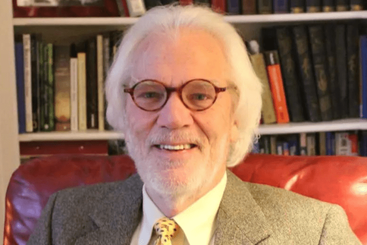 A man poses sitting at a desk inside.