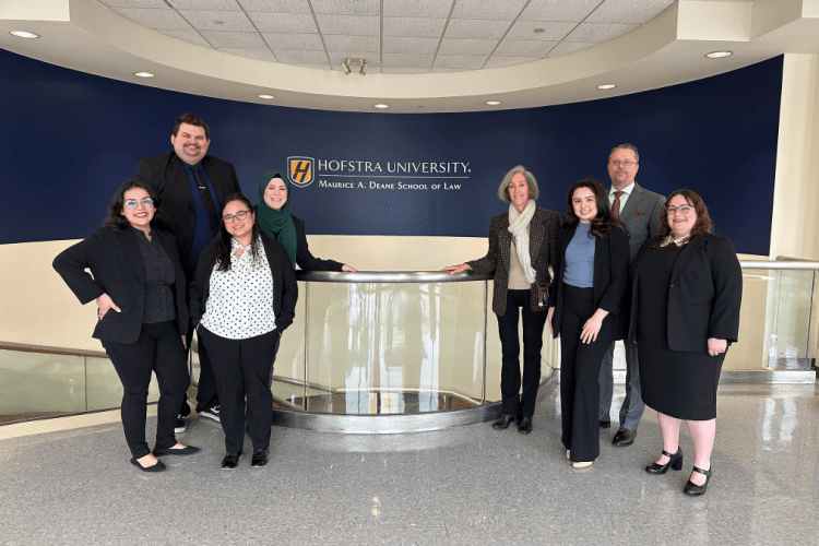 A group of 8 people pose by a sign at a school