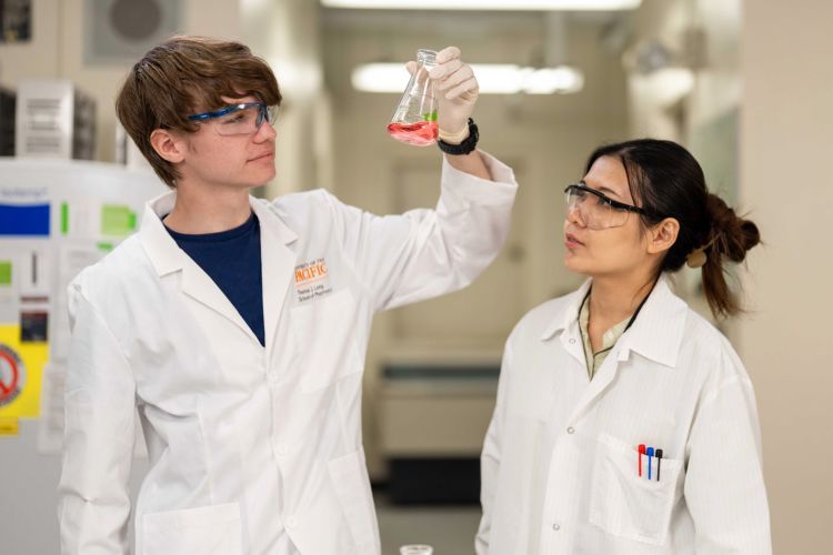 Two students wearing white coats in a research lab