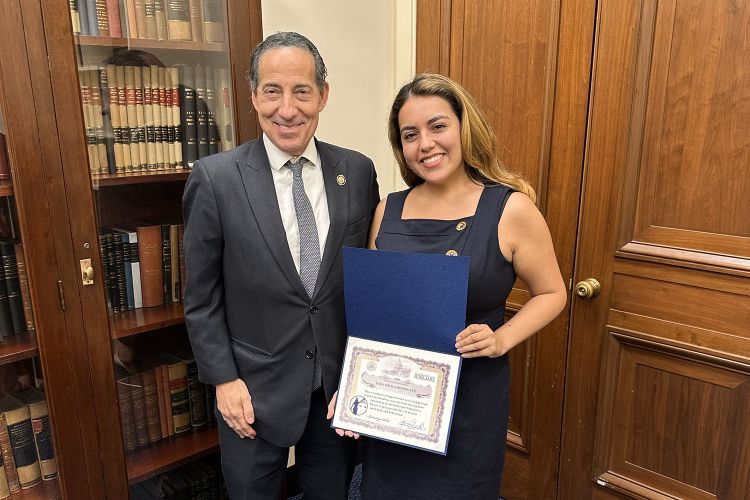 A woman holding a certificate smiles for a photo next to a man in a suit