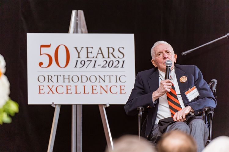Richard Rutter sits in a chair next to a sign that reads 50 years of orthodontic excellence 