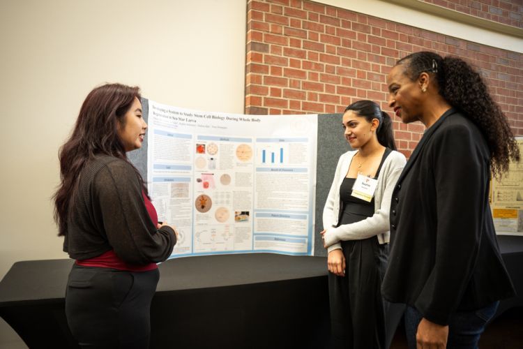 students present research in front of a poster board