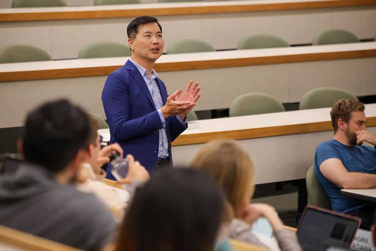 A professor teaching a class with students in the background. 