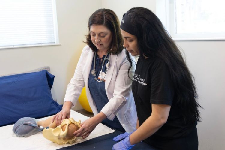 A professor showing a student a midwifery technique with a model 
