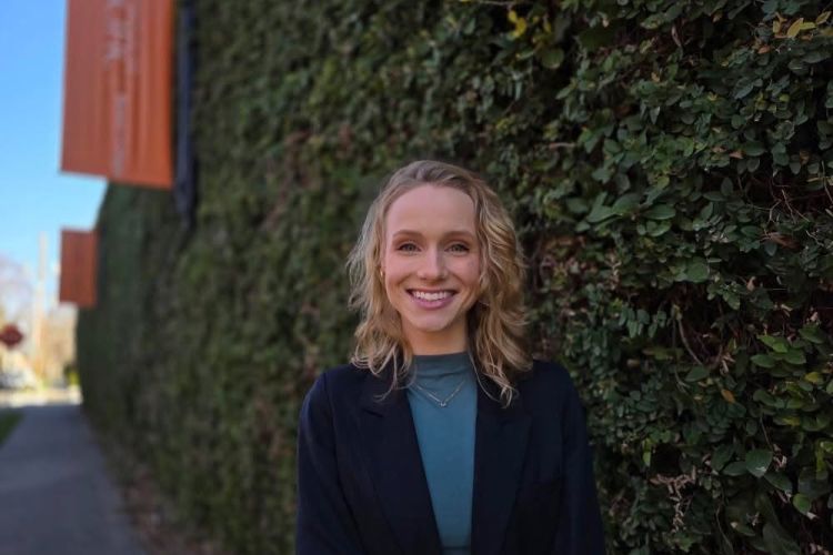 A professional photo of a women smiling standing in front of a greenery background.