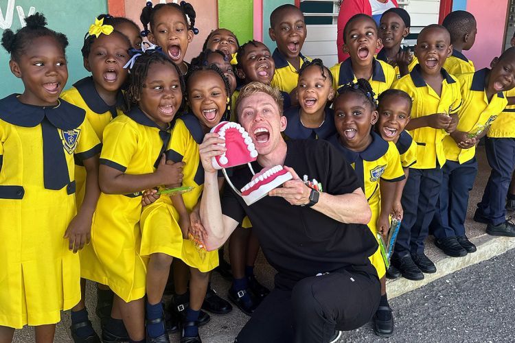 male dental student holding large plastic jaw for teaching the group of children posed with him