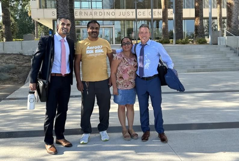 Four people posed together in outdoor setting, smiling at camera. 