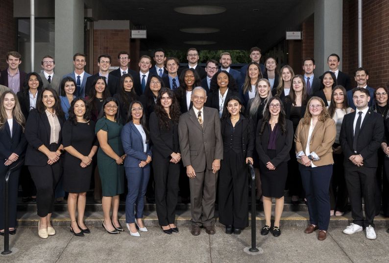 A group of about 40 students wearing suits posing outside