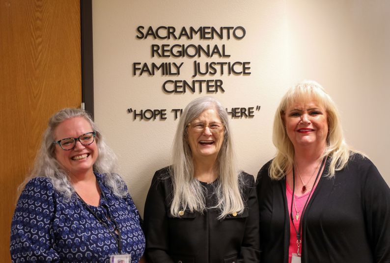Three women stand in front of a sign that says "Sacramento Regional Family Justice Center." 