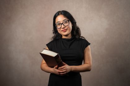A student holding a textbook in front of a neutral background 