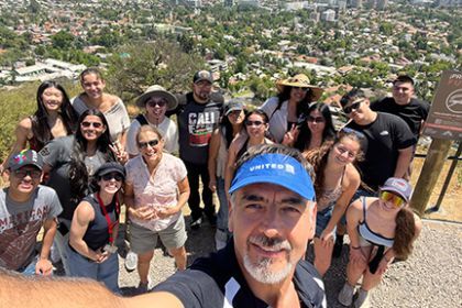 A group of students pose on a mountain top with the city below