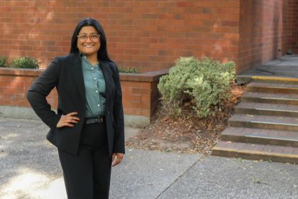 A woman wearing a suit poses for a photo outdoors on a campus