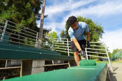 A student adds fresh green paint to a bench.