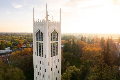 An aerial image of a tall white tower in front of fall foliage.
