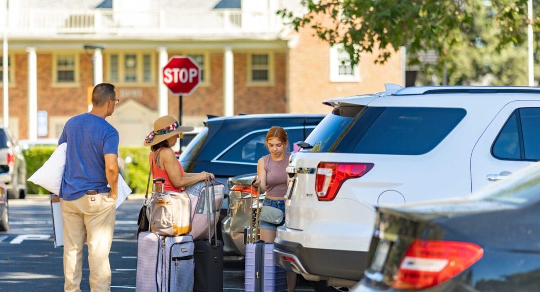 students unload a car in front of a greek house